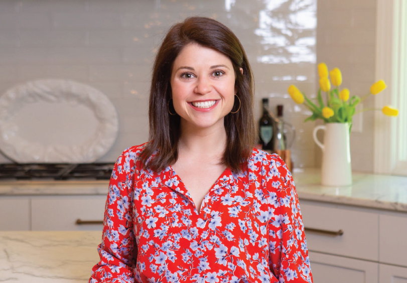 Sophie Dolan, MS, RDN, smiling in a red floral blouse in a modern kitchen with yellow tulips in the background