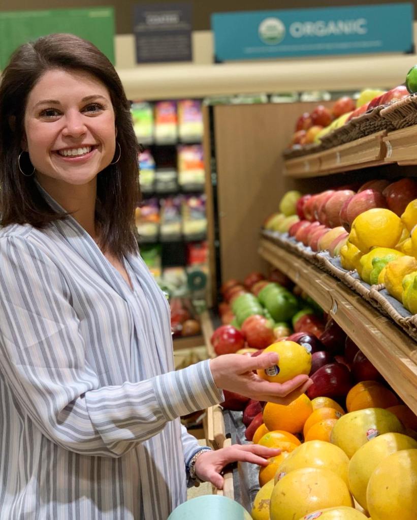 Sophie Dolan MS, RDN, selecting a lemon from the produce section in a grocery store.