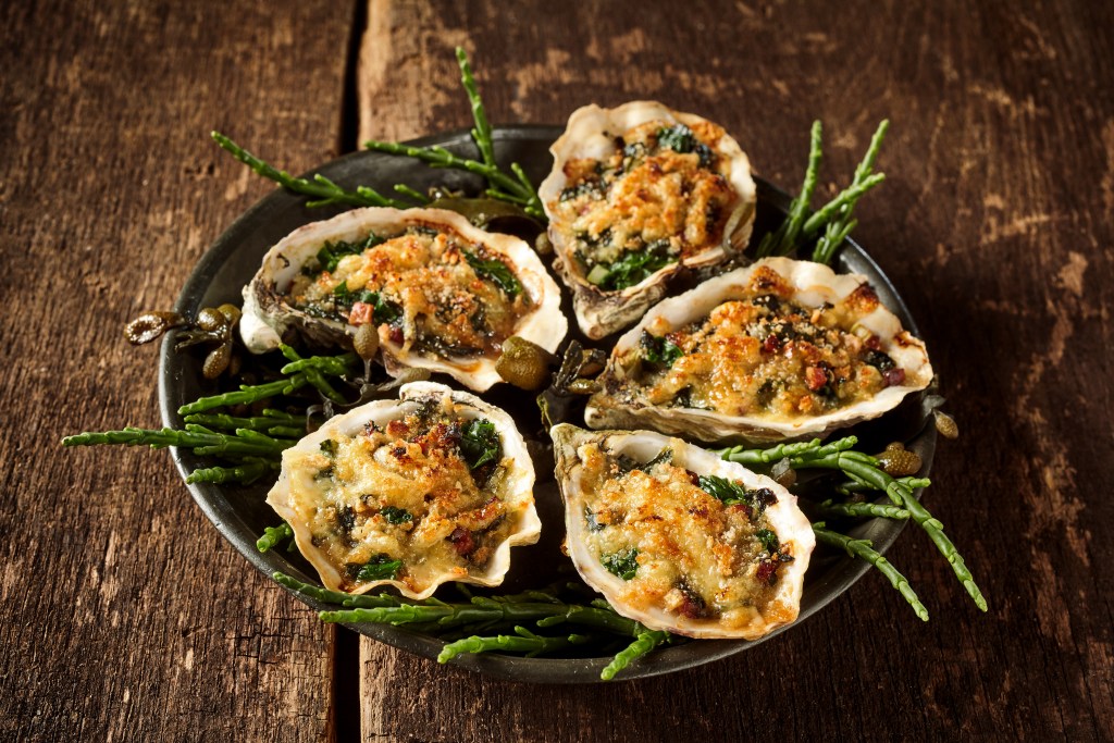 Baked Oyster Rockefeller topped with a rich blend of spinach, breadcrumbs, and melted cheese, served on a rustic plate with fresh greens.