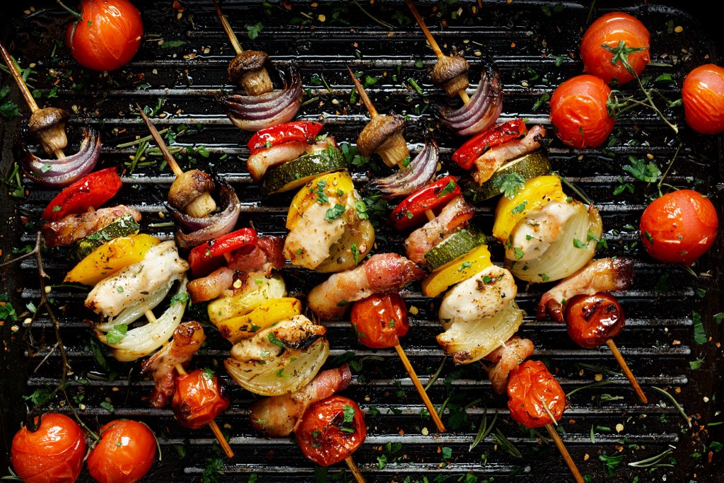 Colorful grilled skewers with chicken, bacon, mushrooms, tomatoes, onions, zucchini, and bell peppers on a barbecue grill