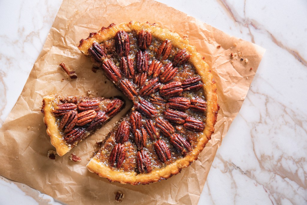 Overhead view of a classic pecan pie with one slice removed, featuring whole pecans arranged on a glossy filling