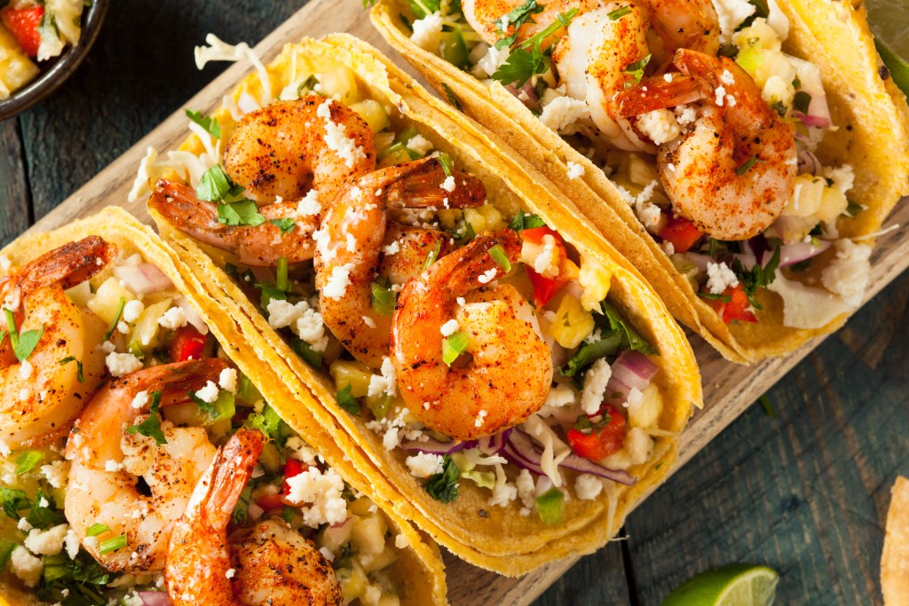 Spiced grilled Gulf shrimp tacos with diced vegetables and crumbled cotija cheese in corn tortillas