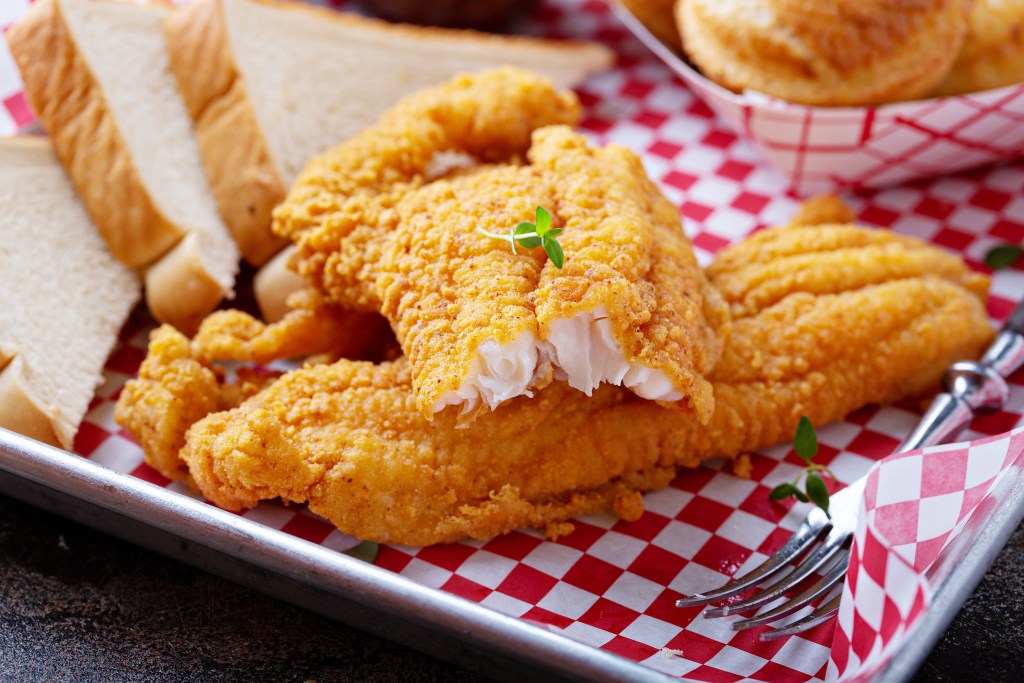 Golden fried catfish fillets served on a tray with sliced white bread and garnished with fresh herbs