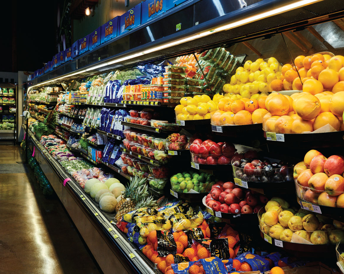 Colorful produce aisle at Piggly Wiggly River Run featuring fresh fruits and vegetables including citrus, apples, greens, and packaged salads