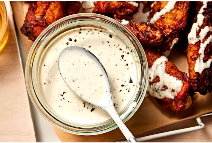 Glass jar of Alabama White Sauce with spoon, served alongside saucy grilled chicken wings