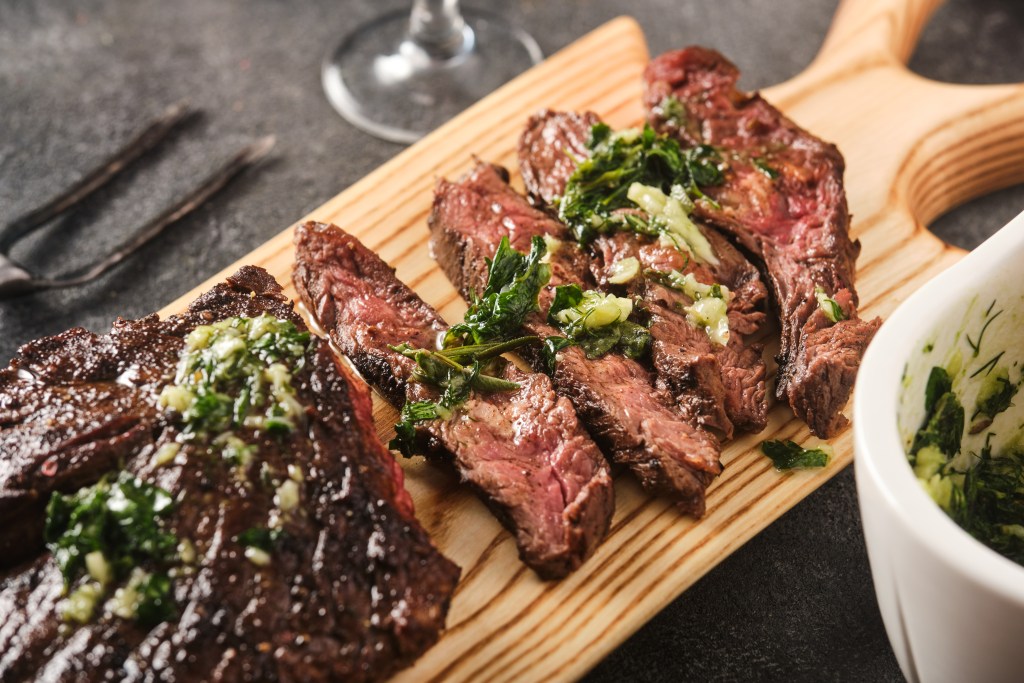Sliced grilled skirt steak topped with fresh herb sauce served on a wooden cutting board