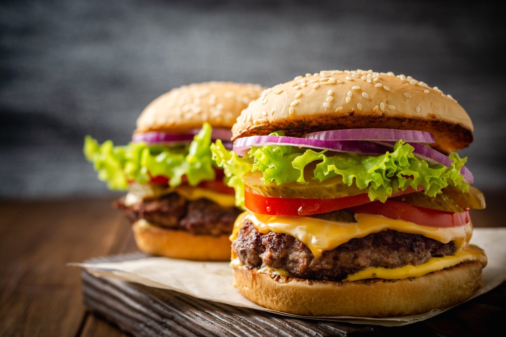 Two juicy cheeseburgers with lettuce, tomato, pickles, onions, and cheddar cheese on sesame buns