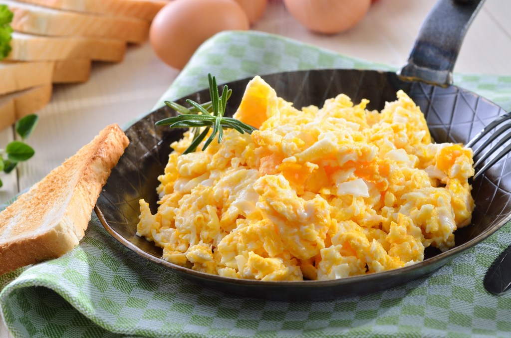 Fluffy scrambled eggs served in a skillet with a side of toasted bread on a green checkered cloth