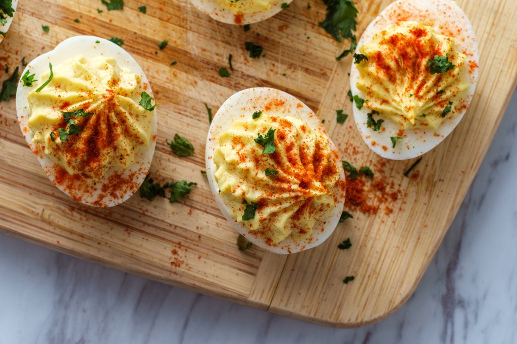 Deviled eggs topped with paprika and chopped parsley on a wooden board