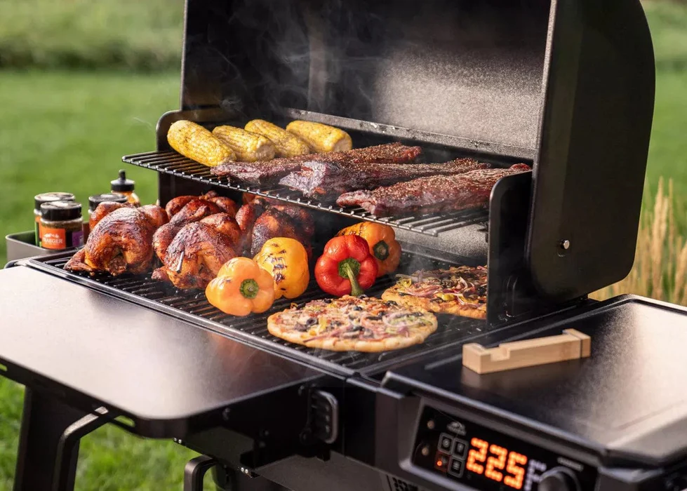 Traeger Woodridge WiFi Grill cooking corn, ribs, whole chickens, bell peppers, and pizzas outdoors