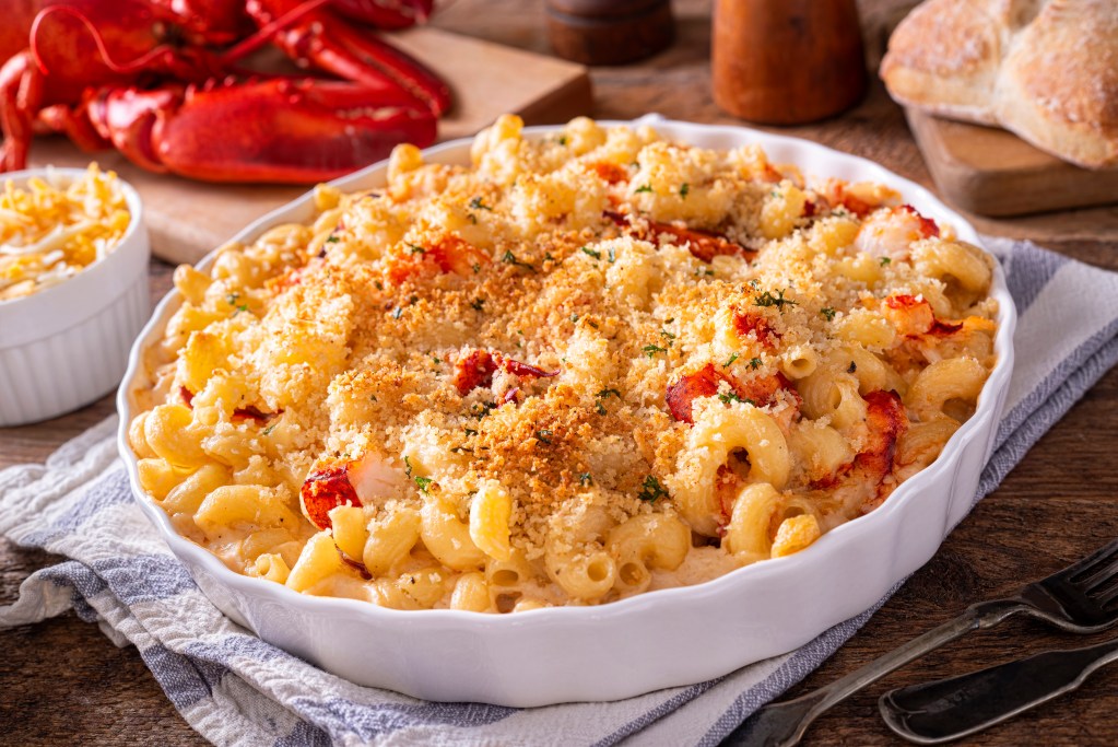 Close-up of baked macaroni and cheese with lobster chunks and a golden breadcrumb topping in a white casserole dish
