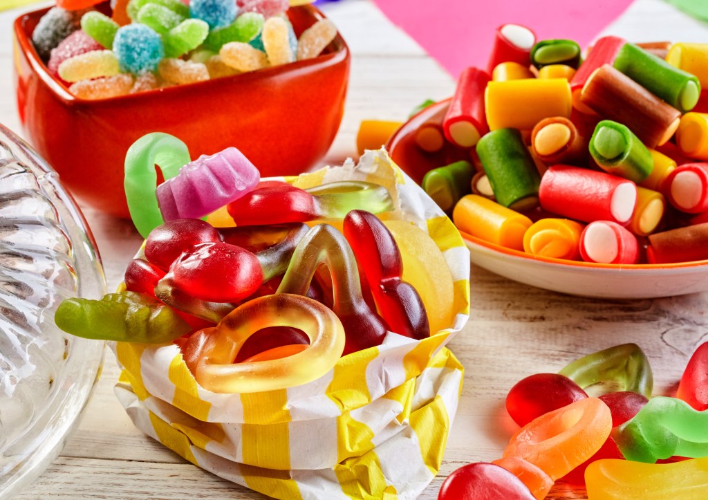 Bowls of colorful gummy rings, sour candies, and licorice pieces on a white wooden table