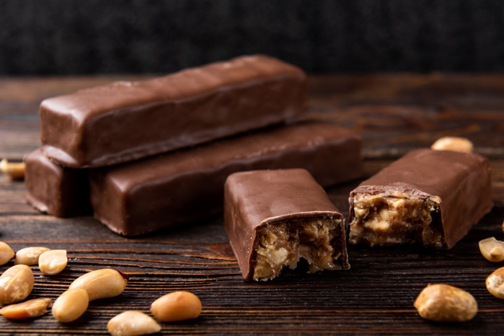 Milk chocolate bars with peanut and caramel filling displayed on a rustic wooden surface