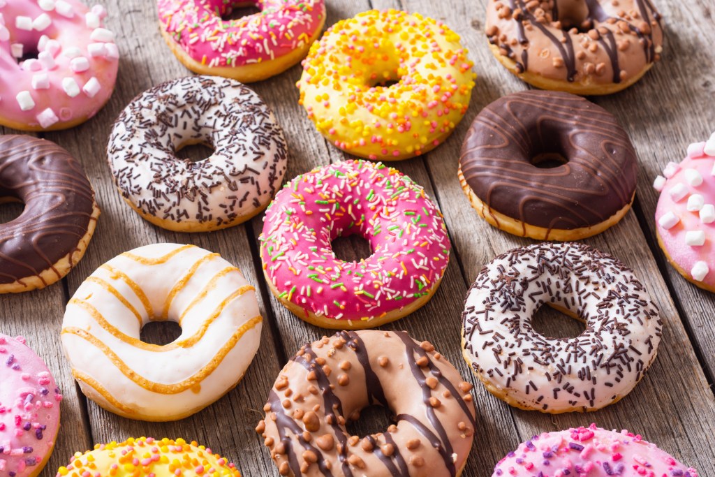Colorful assortment of fresh donuts with chocolate, vanilla, and strawberry frosting, topped with sprinkles and candies on a rustic wooden table