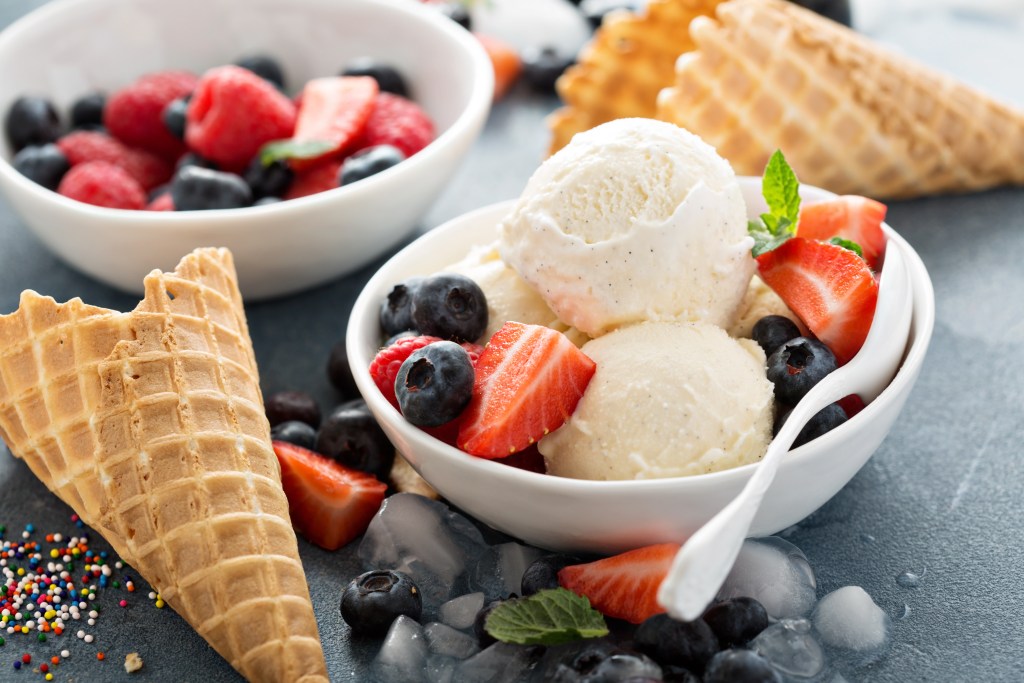 Bowl of vanilla ice cream with strawberries, blueberries, and waffle cones on a dark background