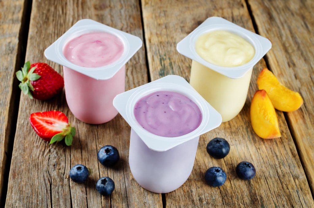 Three cups of strawberry, blueberry, and peach yogurt with fresh fruits on rustic wooden table