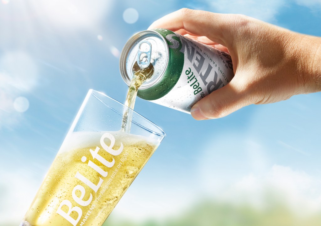 Close-up of BeLite premium light beer being poured from a can into a branded glass outdoors on a bright, sunny day