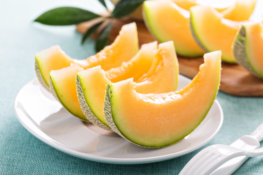 Fresh cantaloupe wedges on a white plate, showcasing their vibrant orange flesh and green rind