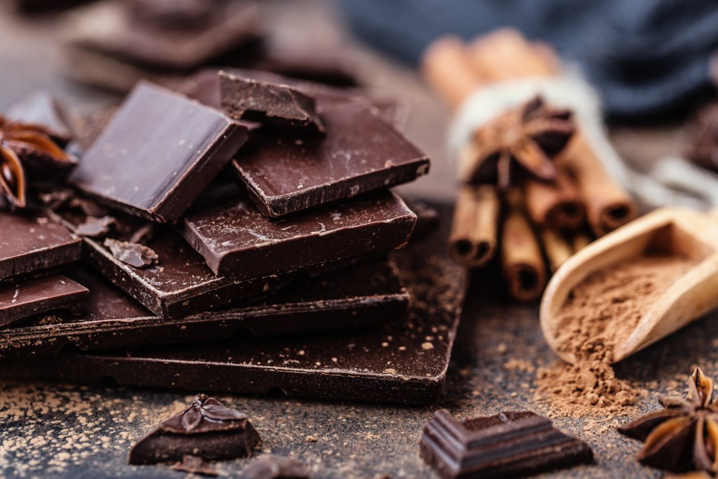 Stack of rich dark chocolate bars with cocoa powder, cinnamon sticks, and star anise on a rustic surface