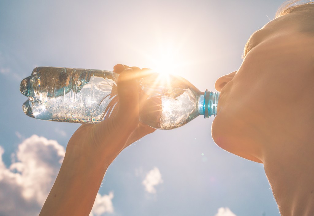 Person drinking water from a plastic bottle under bright summer sunlight