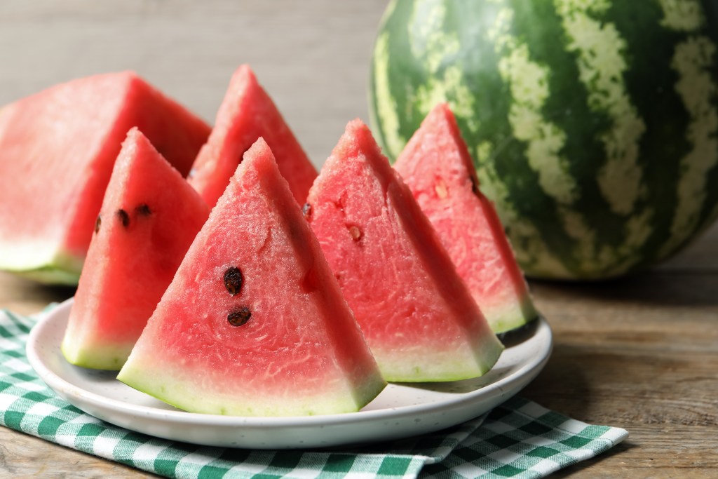 Juicy watermelon wedges arranged on a white plate with a whole watermelon in the background