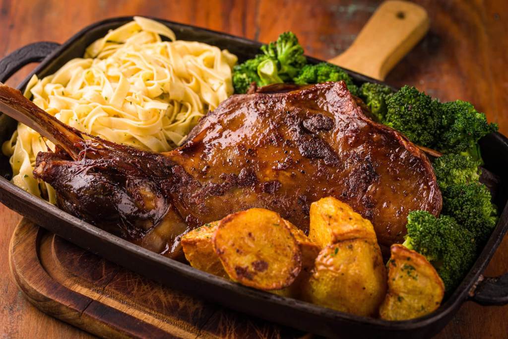 Juicy bone-in pork chop served with fettuccine pasta, roasted potatoes, and steamed broccoli on a wooden table