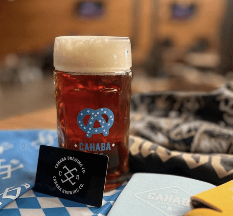 Glass stein of Cahaba Oktoberfest Märzen beer with foamy head, surrounded by branded items and festive decor