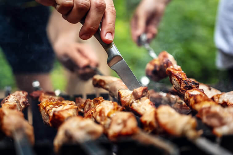 Close-up of people grilling seasoned meat skewers over a charcoal grill during an outdoor barbecue