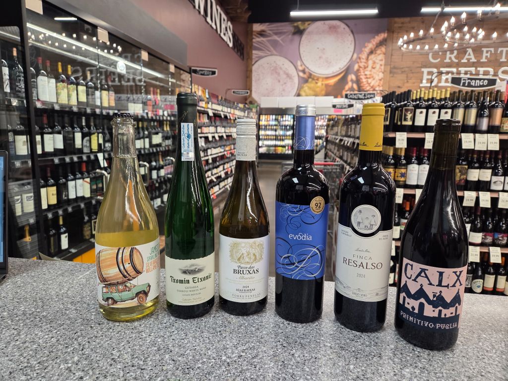 Selection of white and red wine bottles displayed in a wine store aisle promoting a wine tasting event at Bluff Park on June 12