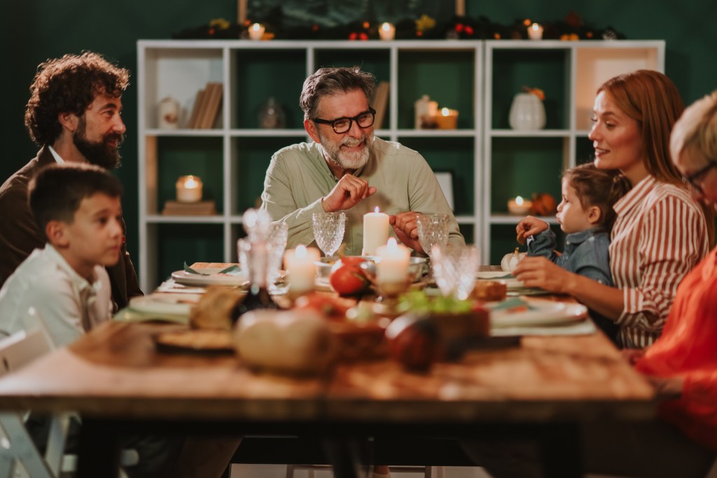 Multi-generational family enjoying Thanksgiving dinner around a warmly lit table with candles and autumn decor