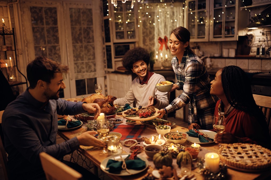 Group of friends sharing a festive holiday dinner at home with roasted turkey, side dishes, and seasonal decorations