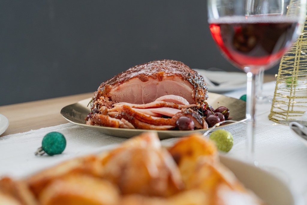 Sliced brown sugar glazed ham served with grapes on a holiday table with wine and festive decorations