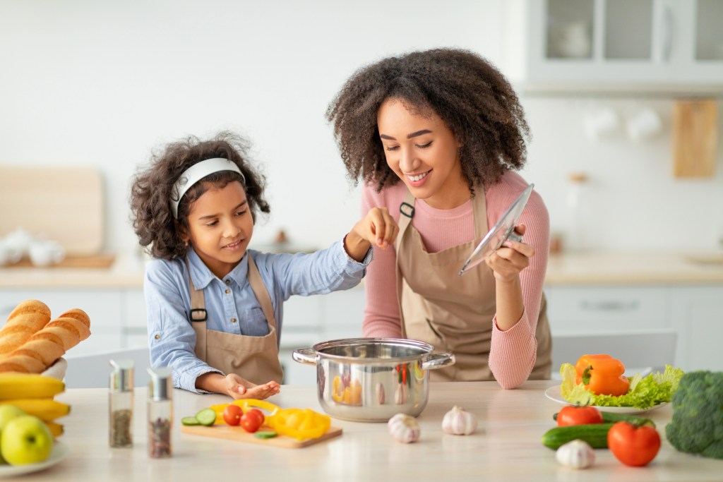 Smiling mother and daughter cooking a one-pot meal with fresh vegetables in a modern kitchen