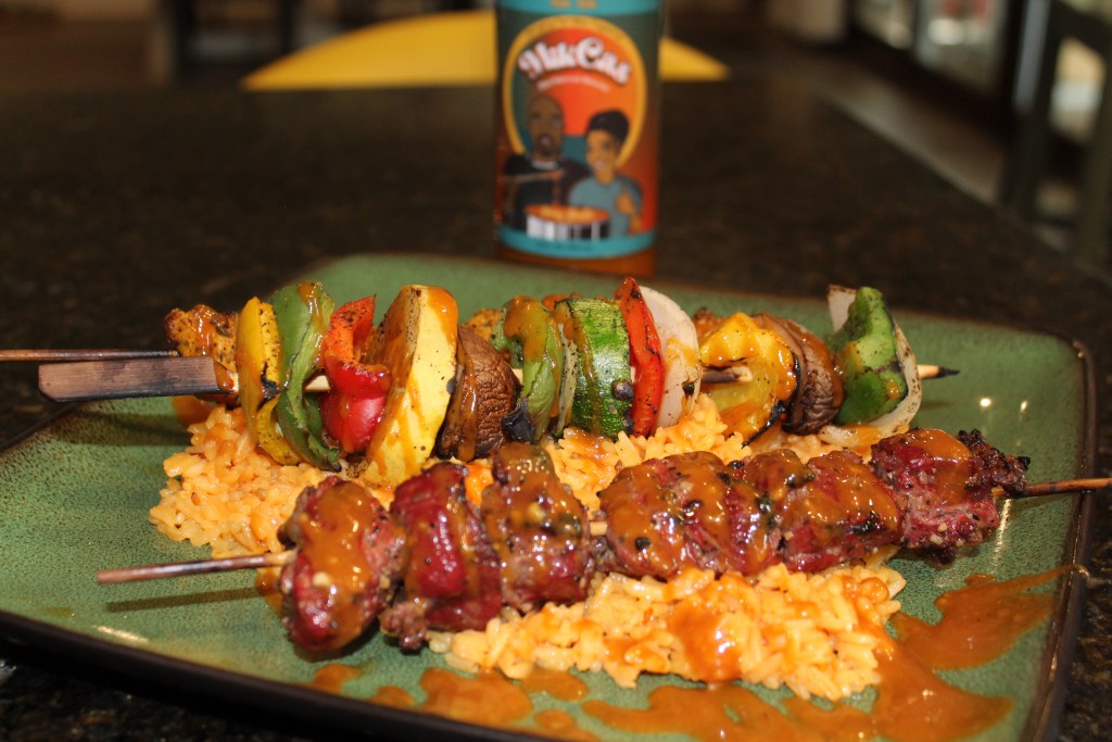 Close-up of grilled beef and vegetable skewers served over seasoned rice, drizzled with MikCas BBQ Sauce