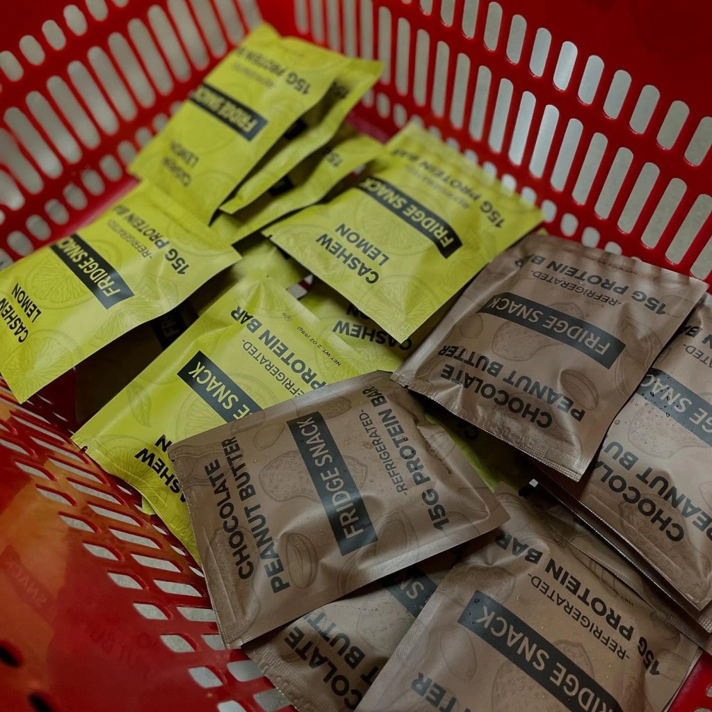 Close-up of assorted Fridge Snack Protein Bars in a red shopping basket at Piggly Wiggly Birmingham, featuring Cashew Lemon and Chocolate Peanut Butter flavors