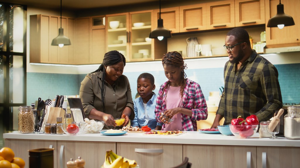 Family preparing homemade pizza together in a modern kitchen with fresh vegetables and ingredients on the counter
