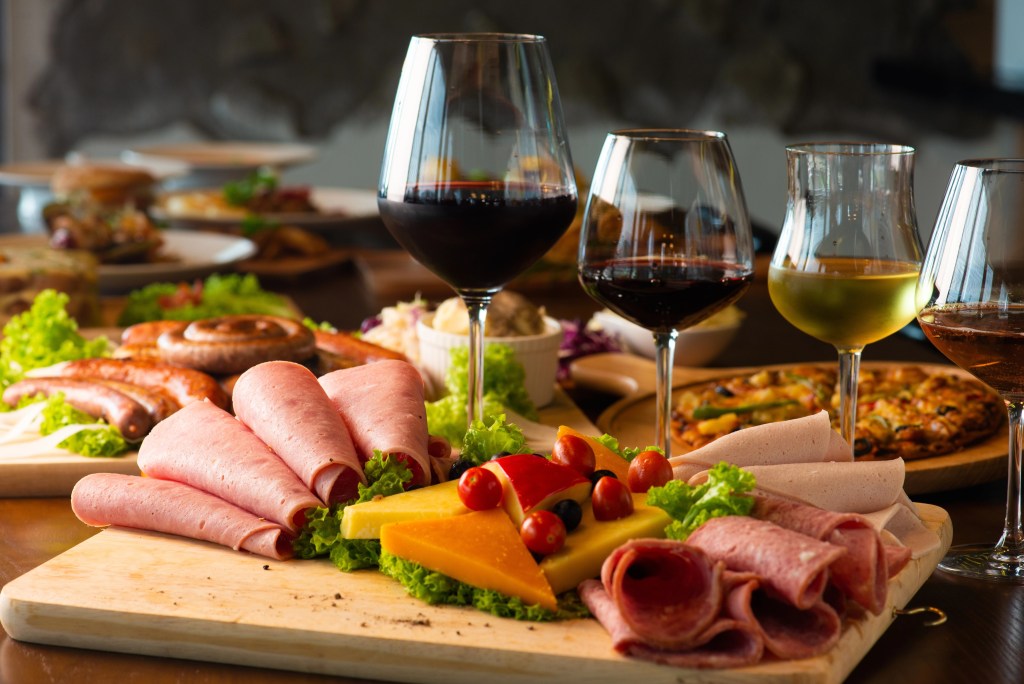 Charcuterie board with sliced cured meats, cheddar cheese, and wine glasses filled with red and rosé wine