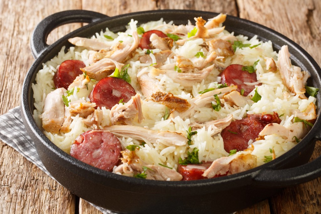 Skillet of long grain white rice with shredded chicken and sliced sausage garnished with herbs on a rustic wooden table