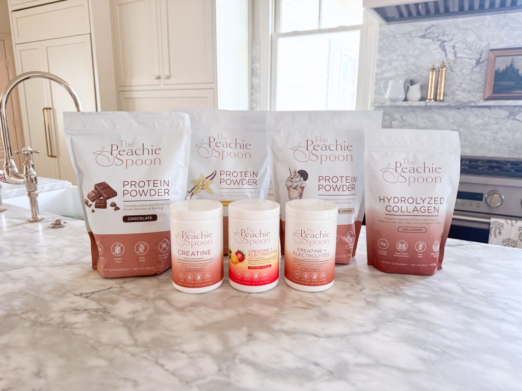 The Peachie Spoon wellness supplement lineup including protein powder, creatine, creatine with electrolytes, and hydrolyzed collagen displayed on a marble kitchen counter