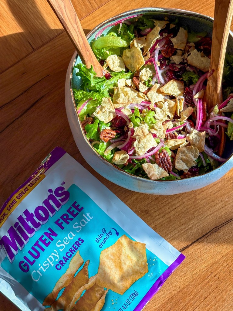 Bowl of fresh salad with pecans cranberries and red onion topped with gluten free crackers next to Milton crackers package