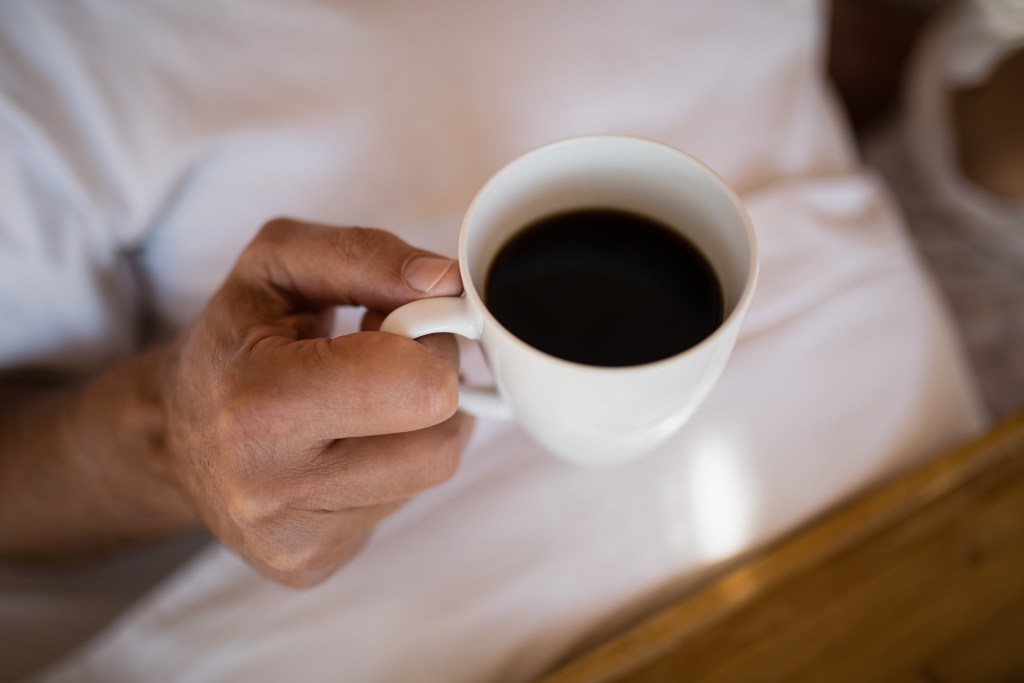Close up of a hand holding a white mug filled with black coffee in a cozy indoor setting