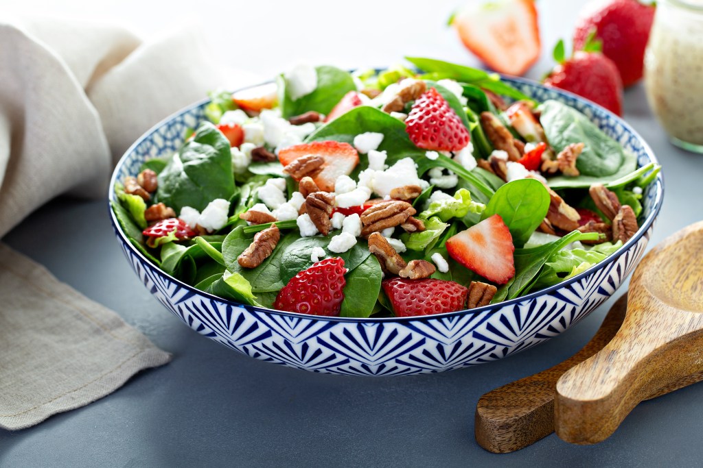 Fresh strawberry spinach salad with feta cheese pecans and leafy greens in a patterned bowl