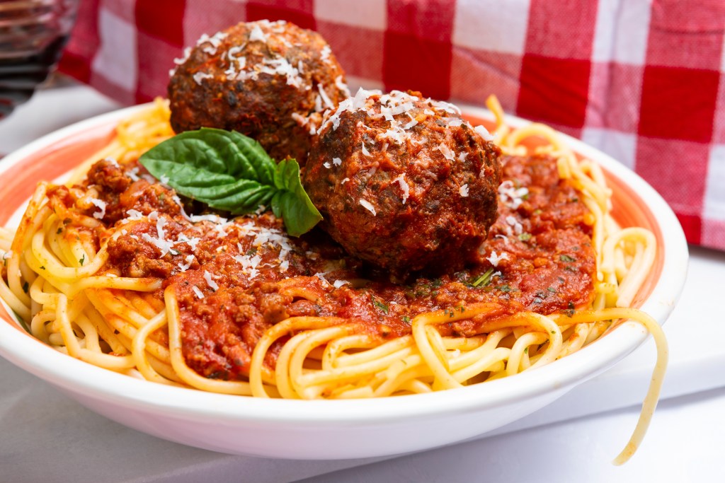Plate of spaghetti topped with rich marinara sauce, large meatballs, grated Parmesan, and fresh basil garnish