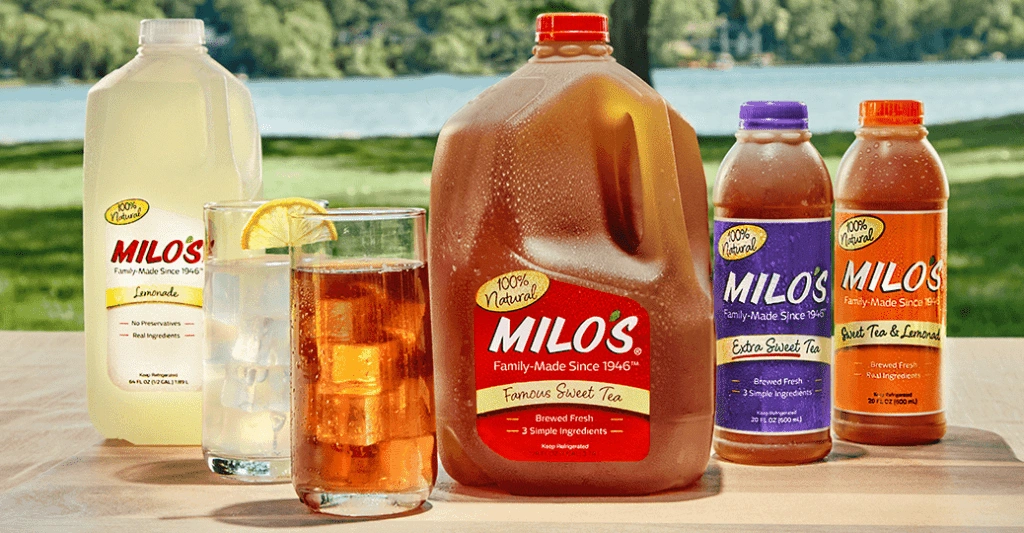Assortment of Milos sweet tea and lemonade bottles with a glass of iced tea and lemon on a table outdoors