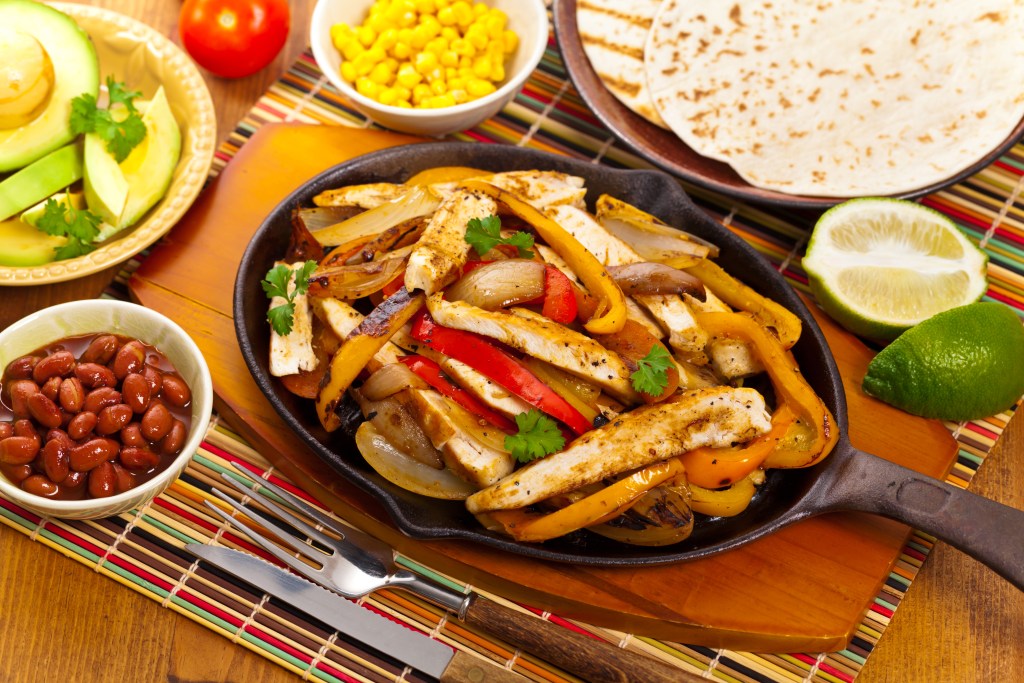 Sizzling skillet of chicken fajitas with grilled bell peppers and onions served with tortillas avocado beans and lime