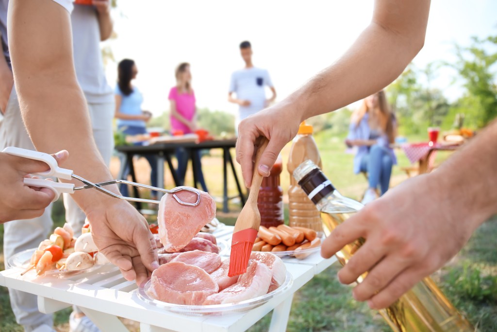 Hands preparing raw meat and cookout ingredients outdoors with Alabama-made foods for a family barbecue gathering