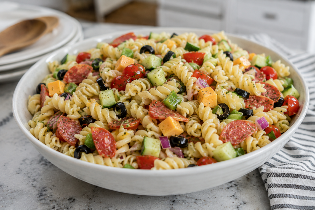 Bowl of classic summer pasta salad made with rotini pasta, cherry tomatoes, cucumbers, cheddar cheese cubes, black olives, red onion, and Italian dressing