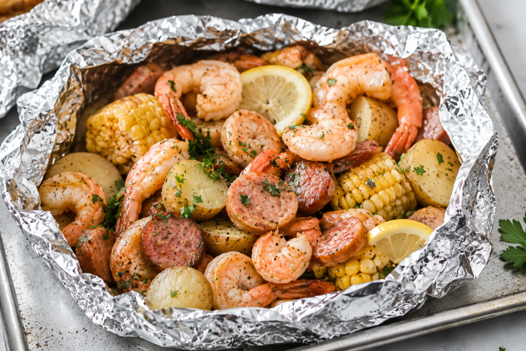 Garlic butter shrimp foil packet with smoked sausage, baby potatoes, corn on the cob, and lemon slices cooked in foil and served on a sheet pan