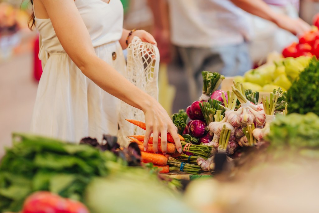 Customer selecting fresh carrots and seasonal vegetables at a Piggly Wiggly produce department during August summer grocery shopping