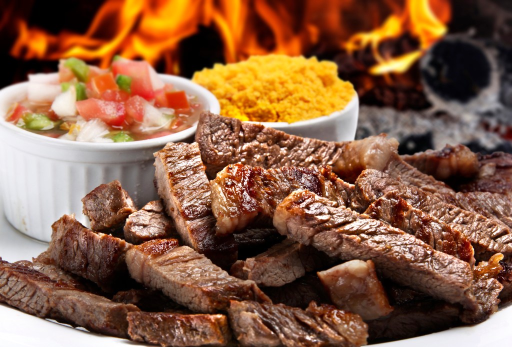 Sliced grilled steak served with fresh salsa and seasoned farofa, showcasing classic barbecue side dishes for a backyard cookout.